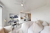 Located at 312 W Republican Street in Seattle's desirable Queen Anne neighborhood, this efficiently designed studio unit makes excellent use of its single-floor layout. The open-plan main area seamlessly integrates the sleeping, living, and kitchen spaces into one cohesive environment, finished with light wood-style flooring and crisp white walls that enhance the sense of openness.

The kitchenette is tucked neatly along one wall, featuring white cabinetry with open shelving, a stainless steel refrigerator, a microwave, a single-basin sink, and recessed lighting overhead. A ceiling fan with integrated lighting keeps the space comfortable year-round. A dedicated workspace with room for a desk sits adjacent to the kitchen area, making the unit well-suited for remote work.

A large picture window floods the living area with natural light and frames impressive elevated views of the Seattle skyline and Elliott Bay waterfront beyond. The bathroom is clean and modern, appointed with a white quartz vanity, under-mount sink, brushed nickel hardware, and a full mirror. A separate closet with a clothing rod and additional storage provides practical organization. Sliding doors and light-toned finishes throughout maintain a cohesive, contemporary aesthetic ideal for urban living.