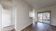 This single-floor residence offers a clean, well-organized layout designed for comfortable everyday living. Throughout the home, wood-style flooring provides a warm, cohesive aesthetic, complemented by crisp white walls and crown molding that lend a polished finish to each room.

The open living area is bright and airy, benefiting from natural light that streams through sliding glass doors leading to a private balcony with outdoor views. The layout flows naturally into the kitchen, which is accessible via a pass-through counter and features dark granite-style countertops, light wood cabinetry, and stainless steel appliances including a range, over-the-range microwave, refrigerator, and dishwasher.

The bedroom is generously proportioned, fitted with a ceiling fan and large windows that invite ample natural light. An adjacent walk-in closet offers extensive wire shelving for organized storage. A secondary room near the entry provides additional flexible living space.

The bathroom is well-appointed with a long vanity, light wood cabinetry, dark countertops, a large mirror, and a separate shower area with tiled walls. The entryway features a mirrored closet and recessed lighting, creating a welcoming first impression. Overall, this residence presents a functional, light-filled living environment with thoughtful design details throughout.