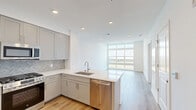 This thoughtfully designed one-bedroom, one-bathroom residence at 2000 Schindler Drive in South Amboy, NJ offers a clean, modern aesthetic throughout. Light-toned hardwood flooring flows seamlessly across the open-concept living and kitchen area, creating a cohesive and airy feel. The kitchen is a standout feature, equipped with grey shaker-style cabinetry, quartz countertops, a herringbone tile backsplash, and a full suite of stainless steel appliances including a gas range, built-in microwave, dishwasher, and a French door refrigerator. A peninsula with an undermount sink adds both functionality and a natural division between the kitchen and living space. Floor-to-ceiling windows in the living area flood the space with natural light and frame expansive outdoor views, with access to a private balcony. The generously sized bedroom features its own large window overlooking the surrounding landscape, continuing the light and airy atmosphere. The bathroom is finished with neutral tile flooring, a vanity with warm wood accents, and a separate shower enclosure. Recessed lighting, crisp white walls, and a clean, contemporary design make this a polished and move-in ready residence.