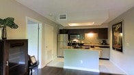 This single-floor space is designed with a practical and modern aesthetic, combining functional layout with contemporary finishes. The kitchen serves as a central highlight, featuring dark espresso cabinetry, granite countertops, and stainless steel appliances including a refrigerator, electric range, and built-in microwave. A peninsula with a granite overhang provides additional prep space and casual seating, while recessed overhead lighting and under-cabinet illumination keep the area well-lit. Dark hardwood flooring runs throughout, creating a cohesive and polished look.

The living area is bright and welcoming, anchored by a large sliding glass door that floods the room with natural light and provides direct access to a private balcony with exterior views. Neutral wall tones complement the space, while a textured area rug adds warmth over the hardwood floor. A separate door visible from the main corridor suggests additional rooms, enhancing the overall functionality of the layout. The textured ceiling and clean white trim are consistent throughout, contributing to a unified and well-maintained interior ambiance.