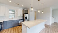 Located at 1290 Old Peachtree Rd NW in Duluth, Georgia, this contemporary two-floor residence showcases a thoughtfully designed interior with high-quality finishes throughout. The open-concept kitchen is a standout feature, boasting a large center island with a crisp white quartz countertop, two-tone cabinetry in white and slate gray with gold hardware, a classic subway tile backsplash, and a full suite of stainless steel appliances. Elegant pendant lighting in brushed brass adds a warm, modern touch overhead. Warm-toned hardwood-style flooring flows throughout the main living areas, complementing the bright, neutral palette. The bedrooms offer plush carpeting and generous natural light through large windows with views of the surrounding greenery and neighborhood. One bedroom features a skylight and direct access to a private balcony, enhancing the sense of openness. The bathrooms are finished with gray shaker-style cabinetry, white quartz countertops, gold-accented hardware, large mirrors, and walk-in glass showers. Throughout the home, clean architectural lines, recessed lighting, and an abundance of windows create an inviting, airy ambiance well-suited for modern living.