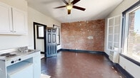 Located at 4077 W 3rd St in the heart of Los Angeles, this studio offers a thoughtfully utilized single-floor layout that combines living, sleeping, and cooking areas into one cohesive space. The main living area is defined by rich, dark hardwood floors and crisp white walls accented by bold black door and window trim, creating a striking visual contrast. A standout feature is the full exposed brick accent wall, which adds warmth, texture, and an industrial character to the space. Natural light flows in generously through multiple windows, including a set of charming French-style casement windows that open to views of the surrounding neighborhood. A ceiling fan overhead provides both function and a classic touch. The compact kitchenette is efficiently designed, featuring a combination cooktop and sink unit, an under-counter refrigerator, and wall-mounted cabinetry for storage. A dedicated closet offers additional storage. The bathroom is bright and clean, finished in white tile with a full tub and shower combination, a vanity with under-cabinet storage, and a window that brings in natural light. The overall ambiance blends vintage character with practical urban living in a central Los Angeles location.