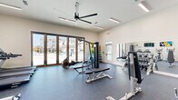 Located at 1000 Banner Dr in Gallatin, Tennessee, this fitness center offers a spacious, single-floor layout designed to support a comprehensive workout experience. The facility features high ceilings with a large industrial-style ceiling fan and recessed linear lighting, creating a bright and airy atmosphere throughout. Durable rubber flooring in a speckled gray finish covers the entire space, providing both comfort and safety during exercise.

The cardio zone is lined with multiple treadmills and elliptical trainers, each positioned in front of wall-mounted flat-screen televisions for an engaging workout experience. The strength training area is well-appointed with a multi-station cable machine, a rowing machine, adjustable benches, and a full rack of dumbbells and kettlebells in varying weights. A plyo box and additional free weights round out the functional training options.

Full-length wall mirrors span one side of the fitness center, amplifying the sense of space and allowing users to monitor their form. Large multi-panel glass doors open toward an outdoor pool area, flooding the space with natural light and providing pleasant views of the surrounding residential community. The clean, white walls and modern equipment give the facility a polished, professional appearance well-suited for daily fitness routines.