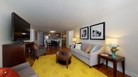 This single-floor residence offers a thoughtfully designed open-concept layout that seamlessly connects the living, dining, and kitchen areas. The living room is a welcoming space anchored by a bold yellow patterned area rug over warm hardwood flooring, complemented by neutral walls, framed artwork, and natural light from multiple windows. The open dining area features a classic table and chair set positioned adjacent to the kitchen, creating an ideal flow for everyday living and entertaining.

The kitchen is well-equipped with rich wood cabinetry, granite-style countertops, stainless steel appliances including a refrigerator, microwave, and dishwasher, and a dual-basin sink. Pendant lighting above the counter island adds a polished touch. Notably, an in-unit laundry area with a full-size washer and dryer is conveniently accessible directly from the kitchen.

The spacious bedroom is finished with plush carpet flooring and features multiple windows that bring in generous natural light. A walk-in closet provides ample storage. Two bathrooms serve the residence — one with a tub and single vanity, and a second, larger bathroom with a dual-sink vanity, walk-in shower, and light tile flooring. Throughout the unit, the design maintains a clean, modern aesthetic with warm, cohesive finishes.