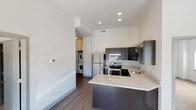 This contemporary single-floor residence showcases a clean, modern design with a cohesive neutral color palette and thoughtfully selected finishes throughout. The open-concept kitchen serves as a central highlight, featuring dark espresso cabinetry with brushed nickel hardware, granite countertops, stainless steel appliances including a refrigerator, electric range, and built-in microwave, and a peninsula that doubles as a breakfast bar. Wood-look flooring extends through the main living and kitchen areas, adding warmth and continuity. Soaring ceilings lend an airy, spacious feel to the living spaces. A dedicated in-unit laundry area with a stacked washer and dryer provides added convenience. The residence includes two bathrooms, each finished with dark cabinetry, granite vanity countertops, tile flooring, and well-lit mirrors. The bedrooms are carpeted for comfort and benefit from large windows that invite natural light and offer views of the surrounding neighborhood. Recessed lighting throughout the main areas ensures consistent, modern illumination. The overall ambiance is clean, functional, and move-in ready, reflecting a well-appointed contemporary design suited for comfortable everyday living.