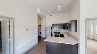 This contemporary single-floor residence showcases a clean, modern design with a cohesive neutral color palette and thoughtfully selected finishes throughout. The open-concept kitchen serves as a central highlight, featuring dark espresso cabinetry with brushed nickel hardware, granite countertops, stainless steel appliances including a refrigerator, electric range, and built-in microwave, and a peninsula that doubles as a breakfast bar. Wood-look flooring extends through the main living and kitchen areas, adding warmth and continuity. Soaring ceilings lend an airy, spacious feel to the living spaces. A dedicated in-unit laundry area with a stacked washer and dryer provides added convenience. The residence includes two bathrooms, each finished with dark cabinetry, granite vanity countertops, tile flooring, and well-lit mirrors. The bedrooms are carpeted for comfort and benefit from large windows that invite natural light and offer views of the surrounding neighborhood. Recessed lighting throughout the main areas ensures consistent, modern illumination. The overall ambiance is clean, functional, and move-in ready, reflecting a well-appointed contemporary design suited for comfortable everyday living.
