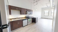 Located in Pittsburgh's South Side neighborhood, this one-bedroom, one-bathroom residence offers a well-appointed layout across a single floor. The kitchen is a standout feature, showcasing striking dark espresso cabinetry that extends toward impressively tall ceilings, complemented by granite-style countertops and a full suite of stainless steel appliances including a refrigerator, electric range, microwave, and dishwasher. Light wood-style flooring runs throughout the kitchen and common areas, adding warmth and continuity to the space. The soaring ceiling height, paired with industrial-style exposed elements and pendant lighting, lends the unit a loft-like character that feels open and airy. The bedroom is carpeted for comfort and features a large window that invites natural light and offers views of the surrounding Pittsburgh cityscape, along with a dedicated closet for storage. The bathroom is clean and functional, featuring a matching dark wood vanity, a white countertop with single-basin sink, a mirrored medicine cabinet, and a full tub/shower combination with chrome fixtures. Light wood-style flooring ties the bathroom's aesthetic together with the rest of the unit. This residence blends modern finishes with an urban industrial character, creating a practical yet stylish living environment in a vibrant Pittsburgh location.