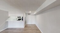 This two-floor residence offers a thoughtfully designed layout that balances functionality and modern style. The main level features an open-concept living area bathed in a clean, neutral palette of white and light gray, with warm wood-look laminate flooring that flows seamlessly throughout. A standout spiral staircase with a sleek metal railing serves as both a functional and architectural focal point, connecting the two levels with visual flair.

The kitchen is positioned adjacent to the living area and features white cabinetry, marble-look countertops, and black appliances including a refrigerator, electric range, and over-the-range microwave. A pass-through counter opens the kitchen to the main living space, enhancing the open feel. The main level also includes a closet with louvered doors and convenient entry storage.

Upstairs, the second floor opens to a spacious landing area with a metal railing overlooking the stairwell, a pendant light fixture, and natural light from a window. This level provides access to a well-appointed bathroom featuring a white vanity, tub-shower combination, and a bright, clean finish. Additional doors on the upper level lead to further private spaces. Textured ceilings are present throughout, adding dimension to the overall interior character.