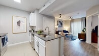 This single-floor residence showcases a clean, contemporary design with a thoughtfully planned open layout. The kitchen serves as a central feature, equipped with white shaker cabinetry, dark quartz countertops, stainless steel appliances including a refrigerator, microwave, and range, and a peninsula with bar seating. A hexagonal tile backsplash adds a stylish detail, while tile flooring ties the kitchen and entryway together seamlessly. The entryway includes a utility panel and keypad-secured front door, offering a practical and secure arrival experience. The open-concept living area flows naturally from the kitchen, featuring wood-look flooring, a ceiling fan, and a large sliding glass door with vertical blinds that allows ample natural light to fill the space. The bedroom is carpeted for comfort and includes a ceiling fan, a door providing access to natural light, and sufficient space for full-sized furnishings. The bathroom features a single vanity with dark cabinetry and white countertop, tile flooring, and a tub-shower combination. Throughout the residence, neutral gray walls and consistent modern finishes create a cohesive and inviting atmosphere well-suited for contemporary living.
