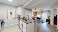 This single-floor residence showcases a clean, contemporary design with a thoughtfully planned open layout. The kitchen serves as a central feature, equipped with white shaker cabinetry, dark quartz countertops, stainless steel appliances including a refrigerator, microwave, and range, and a peninsula with bar seating. A hexagonal tile backsplash adds a stylish detail, while tile flooring ties the kitchen and entryway together seamlessly. The entryway includes a utility panel and keypad-secured front door, offering a practical and secure arrival experience. The open-concept living area flows naturally from the kitchen, featuring wood-look flooring, a ceiling fan, and a large sliding glass door with vertical blinds that allows ample natural light to fill the space. The bedroom is carpeted for comfort and includes a ceiling fan, a door providing access to natural light, and sufficient space for full-sized furnishings. The bathroom features a single vanity with dark cabinetry and white countertop, tile flooring, and a tub-shower combination. Throughout the residence, neutral gray walls and consistent modern finishes create a cohesive and inviting atmosphere well-suited for contemporary living.