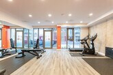 Located at 1424 Highland Rd W in Kitchener, Ontario, this fitness facility offers a well-equipped workout space within a single open-concept floor. The room's design combines functionality with a modern aesthetic, highlighted by bold orange accent walls that contrast with a concrete-effect feature wall and crisp white ceilings fitted with recessed pot lighting.

The flooring transitions between light wood-style vinyl in the central zone and durable rubber matting in the equipment areas, providing both visual appeal and practical protection. A floor-to-ceiling glass window and door frontage faces the street, flooding the space with natural light and offering clear views to the exterior.

The facility is outfitted with a variety of equipment to support diverse training needs. Cardio options include a treadmill and a stationary bike, while strength training is supported by a multi-function cable/pulley machine, an adjustable weight bench, and a well-stocked dumbbell rack with a full range of free weights. A full-length wall mirror enhances the sense of openness and allows users to monitor their form during workouts.

A dedicated entry corridor connects to the main workout area, with a wall-mounted split HVAC unit ensuring year-round climate comfort. The overall layout is efficient and thoughtfully organized, making effective use of the available floor area to deliver a comprehensive amenity fitness space.