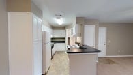 Located at 715 Rice Rd in Ridgeland, Mississippi, this single-floor unit offers a practical and comfortable layout across several well-defined living areas. The kitchen is a standout feature, equipped with ample white cabinetry, dark countertops, a peninsula breakfast bar, a coil-burner electric range with overhead vent hood, a dishwasher, a double-basin stainless steel sink, and a full-size refrigerator. The tile flooring in the kitchen provides easy maintenance, while the generous counter and storage space make it highly functional. The living room is open and inviting, centered around a brick fireplace with a white mantle and accented by a ceiling fan overhead. Neutral-toned carpet flows throughout the living and bedroom areas, lending a warm, cohesive feel to the space. A chandelier adds a touch of elegance to the dining or secondary living area. The bedrooms are carpeted and well-sized, each featuring neutral wall tones and good natural light from windows with outdoor views of greenery. A ceiling fan in one bedroom adds comfort. The bathroom includes a single-sink vanity with a large mirror, a full tub and shower combination, and bright vanity lighting. Overall, the space presents a clean, neutral palette suitable for a variety of furnishing styles.