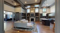 This well-appointed single-story amenity facility showcases refined architectural design, combining classic and contemporary elements throughout its various functional areas. The grand entrance foyer sets an immediate tone of sophistication, featuring soaring ceilings, decorative columns, rich hardwood flooring, and expansive glazed entry doors that draw in abundant natural light.

The central lounge area serves as the heart of the space, anchored by a statement fireplace framed by built-in cabinetry and flanked by transom windows. Coffered ceilings, decorative millwork, and carefully selected furnishings, including plush neutral sectional seating atop a patterned area rug, create an inviting and polished atmosphere.

An adjacent fully equipped kitchen features dark cabinetry, sleek subway tile backsplash, stainless steel appliances, a generous island with white countertops, and pendant lighting. A bright dining nook surrounded by floor-to-ceiling windows offers garden views and a comfortable setting for smaller gatherings.

A secondary lounge area provides a more intimate retreat, with tufted navy seating, a wall-mounted flat-screen television, and a linear fireplace built into a custom niche.

The dedicated fitness center is outfitted with professional-grade cardio and strength equipment, rubber flooring, mirrored walls, and a wide bank of windows overlooking lush outdoor greenery, ensuring a bright and energizing workout environment.