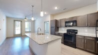 This thoughtfully designed 2-bedroom, 2-bathroom single-floor residence offers a functional and modern living experience. The open-concept kitchen and living area serves as the heart of the home, featuring light wood-style flooring, recessed lighting, and stylish pendant lights above a granite-topped kitchen island with an integrated sink. The kitchen is fully equipped with dark espresso cabinetry, granite countertops, a tile backsplash, and black appliances including a range, microwave, and refrigerator. The living area extends naturally from the kitchen and is illuminated by natural light from windows and a glass door leading to a private outdoor area, complemented by a ceiling fan overhead. The primary bedroom offers plush carpeting, a ceiling fan, and direct access to a well-appointed en-suite bathroom featuring a granite vanity, a glass-enclosed shower, and wood-style flooring. The second bedroom is equally comfortable, with carpeting, a ceiling fan, and a large window allowing ample natural light. The second bathroom includes a soaking tub with clean white subway tile surround. Additional conveniences include two closets and an in-unit laundry area, rounding out this efficiently designed and move-in-ready residence.