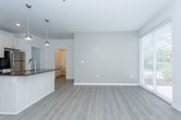 This single-floor unit showcases a contemporary design with a clean, neutral palette carried consistently throughout. The open-concept kitchen serves as the heart of the space, featuring a large center island with a dark countertop and undermount sink, white shaker-style cabinetry extending to the ceiling, and a full suite of stainless steel appliances including a range, microwave, and refrigerator. Pendant lighting above the island adds a modern touch, while recessed ceiling lights ensure even illumination. Light-toned luxury vinyl plank flooring runs through the kitchen and living areas, contributing to a bright, cohesive aesthetic.

The bedrooms are finished with plush neutral carpeting and feature windows dressed with white horizontal blinds that allow natural light to filter in. Each room offers a clean, versatile layout suited to various furniture configurations.

The bathroom is outfitted with a white floating vanity, quartz countertop, undermount sink, and brushed nickel hardware, reflecting a refined, modern sensibility. Light wood-tone flooring ties the bathroom to the rest of the unit seamlessly.

A dedicated laundry area houses a full-size side-by-side washer and dryer, adding practical convenience. Throughout the space, white walls, consistent trim, and recessed ventilation contribute to a polished, move-in-ready environment.