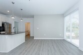 This single-floor unit showcases a contemporary design with a clean, neutral palette carried consistently throughout. The open-concept kitchen serves as the heart of the space, featuring a large center island with a dark countertop and undermount sink, white shaker-style cabinetry extending to the ceiling, and a full suite of stainless steel appliances including a range, microwave, and refrigerator. Pendant lighting above the island adds a modern touch, while recessed ceiling lights ensure even illumination. Light-toned luxury vinyl plank flooring runs through the kitchen and living areas, contributing to a bright, cohesive aesthetic.

The bedrooms are finished with plush neutral carpeting and feature windows dressed with white horizontal blinds that allow natural light to filter in. Each room offers a clean, versatile layout suited to various furniture configurations.

The bathroom is outfitted with a white floating vanity, quartz countertop, undermount sink, and brushed nickel hardware, reflecting a refined, modern sensibility. Light wood-tone flooring ties the bathroom to the rest of the unit seamlessly.

A dedicated laundry area houses a full-size side-by-side washer and dryer, adding practical convenience. Throughout the space, white walls, consistent trim, and recessed ventilation contribute to a polished, move-in-ready environment.