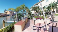Located at 14439 Compass St in Corpus Christi, Texas, this outdoor amenity space offers a vibrant, resort-style environment designed for relaxation and recreation. The grounds are richly landscaped with tall palm trees, tropical plantings, and colorful seasonal flowers, creating a lush coastal atmosphere throughout.

A stamped concrete patio serves as the central gathering area, featuring multiple seating zones with comfortable chairs and tables arranged beneath shaded pergola structures. The outdoor kitchen is a standout feature, equipped with a full-sized stainless steel grill and ample counter space, making it ideal for outdoor entertaining and cookouts.

The resort-style swimming pool is a focal point of the space, surrounded by lounge chairs and bordered by manicured greenery and swaying palms under wide-open Texas skies. Adjacent to the pool, a covered area provides shaded retreat space with additional seating and recreational amenities, including an oversized outdoor Jenga game.

A waterfront patio area offers direct views of the marina and surrounding water, with a dock visible in the background, underscoring the property's prime coastal location. Wrought iron fencing frames the perimeter of the outdoor space, providing security while preserving the open, airy feel. The entire area benefits from abundant natural sunlight and refreshing Gulf Coast breezes, delivering a relaxed, vacation-inspired ambiance year-round.