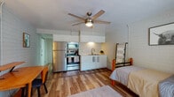 Located at 919 N Stone Ave in Tucson, Arizona, this single-floor studio unit offers a practical and well-appointed open-plan layout that seamlessly integrates the living, sleeping, and kitchen areas into one cohesive space. The interior is defined by painted brick walls that lend a clean, understated character throughout, complemented by warm hardwood-style flooring that runs continuously across the unit.

The kitchenette is efficiently designed with white shaker-style cabinetry, marble-look countertops, and a stainless steel appliance suite that includes a refrigerator, electric range, and over-the-range microwave. A double-basin sink with a pull-down faucet completes the functional cooking area. A ceiling fan with a built-in light fixture is centrally positioned to provide airflow and ambient lighting across the main living space.

The sleeping area accommodates a full-size bed and includes a ladder-style towel or blanket rack. A dedicated workspace features a wood desk with a built-in shelf, a dresser, and decorative wall accents, making the space suitable for studying or remote work. A sliding glass door allows natural light to enter and provides views of the surrounding greenery.

The bathroom is neatly finished with a white vanity, marble-look countertop, a large mirror, and brushed nickel fixtures. Overall, the unit delivers a tidy, modern aesthetic well-suited for efficient single-occupant living in central Tucson.