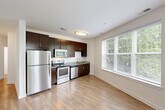 Located at 15955 Frederick Rd in Rockville, MD, this well-appointed three-bedroom, two-bathroom residence offers a comfortable and functional single-floor layout. The open-concept kitchen and living area serves as the heart of the home, featuring rich dark-brown cabinetry, granite-style countertops, and a full suite of stainless steel appliances including a refrigerator, electric range, microwave, and dishwasher. Light hardwood-style flooring runs throughout the main living area, complemented by large windows with blinds that flood the space with natural light and offer leafy, tree-lined outdoor views.

A connecting hallway with flush-mount lighting leads to the three bedrooms, each finished with neutral-toned plush carpeting and windows overlooking the surrounding greenery. Two dedicated closets provide practical storage. The primary bathroom features a granite-topped vanity with dark wood cabinetry, wood-look flooring, and a walk-in shower equipped with grab bars. The secondary bathroom offers a clean, tiled tub-shower combination with brushed gold fixtures and wood-look flooring. The overall aesthetic is modern and neutral, creating a bright, move-in-ready living environment.