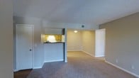 This single-floor residence offers a functional and comfortable layout designed for easy living. The open-concept living and dining area is finished with wall-to-wall carpeting in a warm neutral tone, creating a cohesive and inviting atmosphere throughout the shared space. Soft gray walls and clean white baseboards lend a crisp, understated aesthetic that complements the overall design.

The kitchen is accessible via a convenient pass-through counter with a dark contrasting bar top, which connects it visually to the main living area while maintaining a defined separation. Inside the kitchen, warm honey-toned wood cabinetry lines the walls, and under-cabinet lighting adds a practical, welcoming glow. The layout maximizes efficiency while keeping the kitchen feeling open and connected to the rest of the unit.

A textured ceiling adds subtle architectural character to the space, while recessed HVAC venting ensures climate control is neatly integrated. The neutral tones and simple finishes throughout the unit offer a versatile backdrop, making it easy to personalize with furnishings and décor. The overall ambiance is clean, functional, and well-suited for comfortable everyday living.