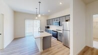 This single-floor residence in Mount Wolf, PA offers a clean, modern aesthetic with a practical open-concept layout. The combined kitchen and living area serves as the heart of the home, featuring warm light wood-style flooring that flows seamlessly throughout the main spaces. The kitchen is well-equipped with slate-gray shaker cabinetry, white quartz countertops, stainless steel appliances, and a central island with a built-in sink illuminated by stylish pendant lighting. A sliding glass door with vertical blinds fills the space with natural light and provides outdoor access. The entryway features durable light wood flooring, a charcoal accent door, and a built-in closet for convenient storage. Both bedrooms are finished with plush wall-to-wall carpeting and ceiling fans, with the primary bedroom offering generous proportions and a dedicated closet. The two bathrooms are designed with accessibility in mind — one features a walk-in shower with grab bars, while the other includes a full tub/shower combo with safety rails and a removable bath bench, both finished in clean white with chrome fixtures.