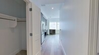 This thoughtfully designed one-bedroom, one-bathroom residence offers a clean, contemporary aesthetic across its efficiently laid-out single floor. Light hardwood flooring flows throughout the main living areas and hallways, creating a warm, cohesive feel.

The kitchen is a standout feature, outfitted with full-height dark wood cabinetry, a striking marble slab backsplash, and a full suite of stainless steel appliances including a gas range, built-in microwave, dishwasher, and French door refrigerator. A dedicated built-in wine cooler sits adjacent to the kitchen near floor-to-ceiling windows that frame expansive urban skyline views, flooding the space with natural light.

The bedroom is a calm, neutral retreat finished with plush grey carpeting and a ceiling fan with integrated lighting. The space is compact yet functional, with clean white walls and ample room for furnishings.

The bathroom is elegantly appointed with large-format marble-look porcelain tile on both the floors and walls. A frameless glass-enclosed walk-in shower features a geometric mosaic tile floor, complemented by a grey wood-tone vanity with a white stone countertop and a matching storage cabinet above.

Two hallways connect the rooms and include closet access, maximizing the practical use of every square foot in this well-appointed urban residence.