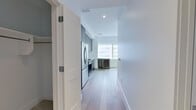 This thoughtfully designed one-bedroom, one-bathroom residence offers a clean, contemporary aesthetic across its efficiently laid-out single floor. Light hardwood flooring flows throughout the main living areas and hallways, creating a warm, cohesive feel.

The kitchen is a standout feature, outfitted with full-height dark wood cabinetry, a striking marble slab backsplash, and a full suite of stainless steel appliances including a gas range, built-in microwave, dishwasher, and French door refrigerator. A dedicated built-in wine cooler sits adjacent to the kitchen near floor-to-ceiling windows that frame expansive urban skyline views, flooding the space with natural light.

The bedroom is a calm, neutral retreat finished with plush grey carpeting and a ceiling fan with integrated lighting. The space is compact yet functional, with clean white walls and ample room for furnishings.

The bathroom is elegantly appointed with large-format marble-look porcelain tile on both the floors and walls. A frameless glass-enclosed walk-in shower features a geometric mosaic tile floor, complemented by a grey wood-tone vanity with a white stone countertop and a matching storage cabinet above.

Two hallways connect the rooms and include closet access, maximizing the practical use of every square foot in this well-appointed urban residence.