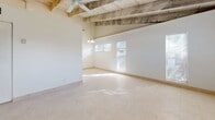 This single-story residence at Azure Villas in Pembroke Park, Florida offers a straightforward and functional layout with notable architectural character. The living area is defined by its distinctive exposed wood beam ceiling, which adds a rustic, structural element to the otherwise clean, white interior. A ceiling fan is mounted overhead, and multiple windows allow natural light to filter into the space, creating a bright and airy atmosphere. Light-toned tile flooring runs consistently throughout the unit, contributing to a cohesive, easy-to-maintain aesthetic.

The kitchen is efficiently organized with white cabinetry extending to the upper walls, providing ample storage. White appliances include a refrigerator, electric range with overhead ventilation, and a dishwasher. Countertop space runs along multiple walls, and a dedicated pantry-style cabinet tower offers additional storage capacity. A ceiling light fixture illuminates the kitchen area.

The bathroom features a vanity with an integrated countertop sink, a wall-mounted mirror, and mirrored sliding closet doors adjacent to the space, enhancing the sense of depth. The toilet is positioned in a separate alcove, and tile detailing is present along the lower walls.

Overall, the unit maintains a clean, minimal presentation with consistent finishes, making it a practical and functional living space.