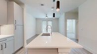 Located at 400 W Main St in Lewisville, TX, this thoughtfully designed one-bedroom, one-bathroom residence offers a clean, contemporary aesthetic throughout its efficiently utilized single-floor layout. The open-concept living area seamlessly integrates the kitchen, dining, and living spaces, all finished with light wood-look flooring that enhances the bright, airy atmosphere. The kitchen serves as a focal point, featuring a large white quartz island with an undermount sink, sleek gray cabinetry, subway tile backsplash, white quartz countertops, and stainless steel appliances including a French door refrigerator. Stylish pendant lighting and a ceiling fan complement the space, while French doors with sidelights open to an outdoor balcony, filling the living area with natural light. The bedroom is carpeted and well-sized, benefiting from a ceiling fan and a large window with outdoor views. It connects directly to a dedicated closet outfitted with built-in shelving and hanging rods for organized storage. The bathroom features a glass-enclosed walk-in shower with elegant tile surround and wood-look flooring. A dedicated laundry area completes this well-rounded residence, offering modern convenience and a cohesive, light-toned design throughout.