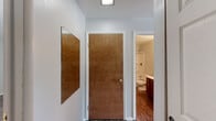 Located at 120 S Kingston Dr in Bloomington, Indiana, this single-floor, one-bedroom, one-bathroom unit offers a functional and cohesive layout designed for comfortable everyday living. Wood-look flooring runs consistently throughout the entire space, lending warmth and visual continuity from room to room. The combined kitchen and living area forms the heart of the unit. The kitchen is equipped with dark cabinetry that contrasts sharply with white appliances, including a refrigerator, electric range, and microwave. Ample counter space and both upper and lower cabinet storage make it highly practical. A sliding glass door in the kitchen area provides access to an outdoor space and allows natural light to filter in. The living room is generously proportioned, featuring light gray walls, multiple windows with blinds, and a clean, open feel. The spacious primary bedroom features notably tall ceilings with high transom-style windows that amplify the sense of airiness, along with an open closet area offering organized storage. The full bathroom includes rich, warm-toned wood vanity cabinetry, a white countertop with a single sink, a large wall mirror, and a full tub-shower combination, all set atop matching wood-look flooring. A connecting hallway ties the layout together efficiently.