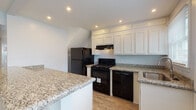 Located at 167 Meadowbrook Lane in Fitchburg, Massachusetts, this two-floor home offers a well-organized layout with thoughtfully updated finishes throughout. The main level centers around an open living area finished with wood-look flooring and recessed lighting, creating a bright, welcoming atmosphere. Natural light filters in through windows overlooking the surroundings, and a staircase with a classic wood and white baluster railing connects the two floors. A closet on the main level provides convenient storage near the living space.

The kitchen is a standout feature, equipped with white shaker-style cabinetry extending to the ceiling, granite countertops with subtle veining, a stainless steel sink, and black appliances including a gas range and dishwasher. A peninsula adds additional counter space and further defines the kitchen area.

Upstairs, multiple carpeted bedrooms are painted in soft blue-grey tones, each offering a calm, neutral atmosphere. Several bedrooms include built-in closets with bifold doors, providing ample storage. The bathroom is finished in clean white subway tile, with a vanity, mirror, and windows that bring in natural light. Recessed lighting is present throughout, contributing to a consistent, polished aesthetic across the entire home.