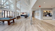 Located at 3960 Independence Dr in Wilmington, NC, this single-story community clubhouse showcases a coastal design aesthetic throughout its expansive, open floor plan. Dramatic vaulted ceilings with exposed white-painted beams and shiplap wall cladding define the main gathering area, which is flooded with natural light through tall floor-to-ceiling windows and sliding glass doors that open to an outdoor pool area beyond.

Light wood-look tile flooring flows throughout the space, transitioning to a herringbone pattern in the co-working zone. The main social area features a lounge with a linear fireplace, built-in shelving with coastal artwork including pelican paintings, and comfortable seating arrangements. A bar counter with bar stools and pendant lighting provides a casual gathering spot alongside open dining tables.

A game room offers a billiards table and foosball table, while a dedicated co-working area provides a large desk with workstations and a mounted flat-screen display. Decorative pendant and globe light fixtures add warmth and character throughout.

A private conference room, finished with a warm wood-paneled ceiling, a substantial conference table, and a statement chandelier, provides an intimate setting for meetings. Coastal-themed artwork and thoughtful furnishings throughout reinforce the relaxed, seaside ambiance of this well-appointed community facility.