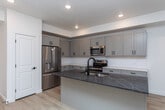 Located at 175 E 1720 N in Heber City, Utah, this well-appointed three-floor home showcases a clean, modern design with thoughtfully selected finishes throughout. The open-concept kitchen serves as a central highlight, featuring gray shaker-style cabinetry with matte black hardware, a large center island topped with dark granite, a built-in sink with a matte black faucet, and a full suite of stainless steel appliances including a refrigerator, range, and microwave. Light-toned hardwood flooring flows through the main living and kitchen areas, lending warmth and continuity to the space. Recessed lighting illuminates each level, creating a bright and welcoming atmosphere throughout. The bedrooms are finished with soft, neutral-toned carpet and feature windows with roller shades that allow for natural light control. Additional rooms with hardwood flooring provide flexible living or utility space. The bathrooms are finished with marble-look tile flooring, white subway-tiled tub surrounds, and matte black fixtures that add a contemporary edge. Vanities with integrated sinks and matching gray cabinetry complete the bathrooms' cohesive aesthetic. The multi-level layout, connected by a staircase visible in the floor plan, offers well-defined zones for living, sleeping, and additional use, making this Heber City home a functional and stylish residence.