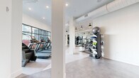 Located at 1647 E Colonial Dr in Orlando, FL, this contemporary fitness center offers a generously sized, single-floor layout designed to accommodate a full spectrum of workout needs. The space is organized into distinct training zones, each thoughtfully equipped and visually distinct.

The cardio zone features multiple treadmills, elliptical machines, a stair climber, and a rowing machine, positioned along expansive floor-to-ceiling windows that frame views of the outdoor pool and surrounding landscaping, allowing natural light to flood the interior. Ceiling fans overhead enhance airflow and comfort during workouts.

The strength training area is well-appointed with a comprehensive rack of dumbbells, adjustable benches, cable machines, and various functional fitness equipment including stability balls and resistance accessories. Full-length mirrors line the walls, amplifying the sense of space.

A dedicated functional fitness zone features bold, colorful wall murals that add an energetic, artistic character to the space. Exposed ductwork and pendant lighting contribute to an industrial-modern aesthetic, while polished concrete-style flooring ties the entire facility together with a clean, professional finish.

The high ceilings, open layout, and abundance of natural light create an inviting and motivating environment, making this fitness center a standout amenity at its Orlando location.