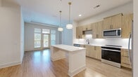 Located at 525 Sawnee Village Boulevard in Cumming, GA, this well-designed 2-bedroom, 2-bathroom residence offers a clean, modern aesthetic across a single-level floor plan. The open-concept kitchen serves as the heart of the home, showcasing light wood-toned cabinetry, a white quartz-topped island with built-in shelving, a textured tile backsplash, stainless steel appliances, and stylish pendant lighting with brass accents. Light hardwood-style flooring extends throughout the main living areas, enhancing the bright, airy atmosphere. The living area benefits from large glass doors that invite natural light and offer outdoor views. Both bedrooms feature plush carpeting and generous windows with exterior views, maintaining a calm and comfortable feel. The spacious primary bedroom includes a walk-in closet fitted with wire shelving systems for ample storage, joined by a second closet of similar design. Both bathrooms are finished with large-format tile flooring, gray cabinetry, white countertops, and framed mirrors. One bathroom features a soaking tub and shower combination, while the other offers a sleek, functional layout. A connecting hallway ties all rooms together efficiently, completing a thoughtfully organized and move-in-ready home.