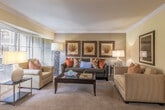 Located at 2400 Yorktown St in Houston's Galleria area, this single-floor residence offers a thoughtfully designed layout that balances comfort and functionality. The living room serves as the heart of the home, featuring plush carpeting, crown molding, and warm neutral tones accented by earthy orange décor. A large bay window floods the sitting area with natural light and offers pleasant views of the surrounding greenery, creating an inviting retreat.

The galley-style kitchen is efficiently organized with white cabinetry, ample counter space, a double sink, and full appliances including a range and refrigerator. Stone-look tile flooring adds durability and visual appeal. Adjacent to the kitchen, a cozy dining nook accommodates a round table with seating for two, framed artwork adorning the walls above.

The bedrooms are carpeted and comfortably sized, each featuring built-in closets with shelving, ceiling fans, and windows dressed with light-filtering curtains that allow natural light to brighten the rooms. The bathroom is clean and well-lit, featuring a vanity with under-sink storage, a large mirror, and tile flooring that complements the overall aesthetic of the home.

Crown molding details and a consistent warm color palette throughout lend the space a cohesive, polished character.