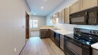 Located at 2106 Runestone Ave in Alexandria, Minnesota, this efficiently designed single-floor unit makes excellent use of its compact footprint. The open kitchen is a standout feature, outfitted with two-tone cabinetry — light upper cabinets paired with darker lower units — light stone countertops, a double-basin sink, and a full suite of black appliances including an electric range, dishwasher, microwave, and refrigerator. Recessed lighting and light wood-look flooring throughout lend the kitchen a clean, modern aesthetic. The kitchen flows naturally into the living area, which benefits from a window that brings in natural light and adds a sense of openness to the space. The full bathroom is thoughtfully finished with a dark wood vanity, white countertop, a well-lit mirror with a contemporary light bar, and a full tub-shower combo, all complemented by the same light wood-look flooring. A dedicated laundry area houses a stacked washer and dryer unit, offering convenient in-unit laundry. Two closets provide ample storage throughout the space. The consistent use of warm wood tones and neutral wall colors creates a cohesive, welcoming atmosphere from room to room.