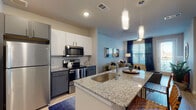 This thoughtfully designed single-floor residence offers a cohesive blend of modern finishes and functional living spaces. The open-concept kitchen is a standout feature, showcasing granite countertops, a large center island with a stainless steel sink and bar seating, white and dark gray two-tone cabinetry, and a full suite of stainless steel appliances including a refrigerator, electric range, and built-in microwave. Pendant lighting adds a refined touch above the island. Light hardwood-style flooring flows seamlessly throughout the unit, connecting each space with a warm, consistent aesthetic.

The living area is bright and welcoming, featuring large windows with navy drapery that invite natural light while a ceiling fan enhances comfort. A private exterior door provides convenient outdoor access directly from the living room.

The bedroom is a serene retreat, anchored by a bold teal accent wall and generous windows dressed in sheer curtains that filter soft, natural light. The en-suite bathroom is well-equipped with a dual-sink granite vanity, dark gray cabinetry, framed mirrors, and direct access to a spacious walk-in closet with built-in shelving and hanging storage. Every detail of this residence reflects a clean, contemporary design sensibility.