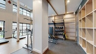 Located at 2022 N Beckley Ave in Dallas, TX, this two-level fitness center offers a comprehensive workout facility spread across two floors. The main level features light hardwood flooring throughout the open cardio and functional training zone, where large industrial-style windows flood the space with natural light and provide views of the surrounding area. Soaring ceilings with exposed beam accents lend an airy, loft-like ambiance to the main floor, which is further highlighted by a striking full-height athletic mural and pendant rope lighting with gymnastic rings suspended overhead.

A sleek black spiral staircase serves as both a functional and architectural centerpiece, connecting the main level to the upper floor. The strength training area is defined by darker, carpet-tiled flooring and features teal accent walls with floor-to-ceiling mirrors that amplify the sense of space. Built-in wood shelving provides organized storage for free weights and accessories, while a full rack of dumbbells and an adjustable bench offer dedicated strength training options.

The upper level provides additional equipment space and overlooks the main floor below. Throughout both levels, recessed lighting and modern finishes maintain a clean, contemporary aesthetic, making this fitness center a highly functional and visually dynamic space.