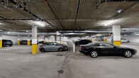 Located at 5460 Fountain Ave in the heart of Los Angeles, this substantial underground parking garage offers an impressively large single-level layout designed to accommodate a significant number of vehicles. The structure is built with robust concrete construction throughout, featuring a exposed concrete ceiling supported by a grid of columns distinctively marked with yellow and red safety striping for clear visibility and driver guidance.

The facility is well-lit by a series of overhead fluorescent strip lighting, ensuring consistent illumination across the entire floor. The ceiling is lined with an extensive network of mechanical infrastructure, including HVAC ductwork, piping systems, and electrical conduit, all of which are openly routed to allow for ease of maintenance and serviceability.

The concrete floor is divided into clearly marked parking bays, with wide drive aisles providing smooth traffic flow throughout the space. A ramped entry and exit point connects the garage to street level, featuring a gated access point for security. Interior access doors are also present, providing connectivity to adjacent building areas. The overall layout is functional and efficiently organized, making this a highly practical parking facility well-suited to serve a high-density residential or commercial building in the Los Angeles area.