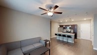 This single-story unit offers a thoughtfully designed open-concept layout connecting the living area and kitchen. The living space features wood-look flooring, neutral-toned walls, and a ceiling fan with integrated lighting. The kitchen is well-appointed with rich dark wood cabinetry, granite countertops, stainless steel appliances including a refrigerator, range, and microwave, and a peninsula island with bar seating illuminated by pendant lighting. Recessed ceiling lights provide additional brightness throughout.

The bedrooms are carpeted for comfort, each featuring ceiling fans with light fixtures, standard closets with sliding or hinged doors, and windows dressed with horizontal blinds that allow natural light. One bedroom includes direct access to a bathroom, enhancing convenience.

The bathroom is efficiently laid out with a dark wood vanity, a wide mirror with overhead lighting, and a full-size soaking tub with a shower combo featuring chrome fixtures and a white surround. Consistent neutral tones throughout the unit create a clean, cohesive aesthetic that balances modern finishes with everyday practicality.