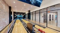 This 1,310 square foot space in Jersey City showcases a unique blend of urban chic and recreational functionality. The venue features a state-of-the-art bowling alley with sleek lanes and electronic scoring displays. Adjacent to the bowling area, a spacious lounge offers a comfortable retreat with plush seating arrangements and a stylish coffee table.

The interior design harmoniously combines industrial and contemporary elements. Exposed brick walls add character and warmth, while floor-to-ceiling windows flood the space with natural light and offer breathtaking views of the city skyline. The ceiling is adorned with modern lighting fixtures, creating an inviting ambiance.

The open floor plan seamlessly integrates various functional areas. A bar area with high stools provides additional seating, while a separate section features tables and chairs for dining or casual meetings. The space is equipped with modern amenities, including large-screen TVs and climate control systems.

Light wood flooring throughout adds warmth and ties the different areas together. The thoughtful layout and versatile design make this space ideal for various events, from casual gatherings to corporate functions, offering a unique blend of entertainment and sophistication in the heart of Jersey City.