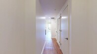This thoughtfully designed 2-bedroom, 1-bathroom residence offers a clean, modern aesthetic throughout its single-floor layout. Warm hardwood-style flooring runs consistently across all living areas, complementing the crisp white walls and creating a cohesive, inviting atmosphere.

The open kitchen and living area serves as the heart of the home, featuring a contemporary kitchen equipped with stainless steel appliances, including a gas range, microwave, and full-size refrigerator. Sleek two-tone cabinetry — combining white upper cabinets with rich wood-toned lower units — frames a white quartz countertop and a peninsula with an undermount sink, ideal for casual dining or food preparation. Recessed and pendant lighting add a polished finishing touch.

Both bedrooms are generously proportioned and bathed in natural light through large windows that frame urban cityscape views. The primary bedroom offers access to an outdoor space, while the second bedroom features a wide window overlooking the surrounding neighborhood. A well-lit hallway with louvered-door closet storage connects the living areas to the bedrooms.

The full bathroom is finished with dark tile surround in the tub-shower combo, a white vanity with quartz countertop, and chrome fixtures, striking a clean, modern balance. Two hallways provide efficient circulation throughout the residence.
