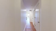 This thoughtfully designed 2-bedroom, 1-bathroom residence offers a clean, modern aesthetic throughout its single-floor layout. Warm hardwood-style flooring runs consistently across all living areas, complementing the crisp white walls and creating a cohesive, inviting atmosphere.

The open kitchen and living area serves as the heart of the home, featuring a contemporary kitchen equipped with stainless steel appliances, including a gas range, microwave, and full-size refrigerator. Sleek two-tone cabinetry — combining white upper cabinets with rich wood-toned lower units — frames a white quartz countertop and a peninsula with an undermount sink, ideal for casual dining or food preparation. Recessed and pendant lighting add a polished finishing touch.

Both bedrooms are generously proportioned and bathed in natural light through large windows that frame urban cityscape views. The primary bedroom offers access to an outdoor space, while the second bedroom features a wide window overlooking the surrounding neighborhood. A well-lit hallway with louvered-door closet storage connects the living areas to the bedrooms.

The full bathroom is finished with dark tile surround in the tub-shower combo, a white vanity with quartz countertop, and chrome fixtures, striking a clean, modern balance. Two hallways provide efficient circulation throughout the residence.