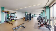 Located at 570 North 5th Street in Philadelphia's Northern Liberties neighborhood, this generously sized fitness center spans a single floor and offers a comprehensive workout environment designed to meet a wide range of training needs. The space is defined by its open, elongated layout, durable speckled rubber flooring, and a clean, modern aesthetic featuring white walls accented by bold teal structural columns that lend a striking visual identity throughout.

Linear LED lighting runs along the ceiling, providing consistent, even illumination across the entire facility. Floor-to-ceiling windows along one side of the space flood the interior with natural light and offer sweeping panoramic views of the Philadelphia skyline, creating an energizing atmosphere for cardio workouts. A dedicated cardio zone lines this window wall, featuring rows of treadmills, elliptical trainers, and stationary cycling bikes, each positioned to take advantage of the city views. Mounted flat-screen televisions provide additional entertainment options.

The strength training area is well-equipped with cable machines, a multi-functional power rack, free-weight stations, and a comprehensive dumbbell rack. A functional training zone includes battle ropes, resistance bands, kettlebells, plyo boxes, and a full rig system. Full-length mirrors are strategically placed throughout to support proper form. The facility offers ample open floor space, supporting a smooth and efficient training experience.