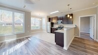 Located at 191 Waters Edge Cir in Waynesville, NC, this well-appointed single-story home offers three bedrooms, three full bathrooms, and a thoughtful layout designed for comfortable everyday living. The open-concept kitchen is a standout feature, showcasing rich dark cabinetry, granite countertops, stainless steel appliances, a peninsula with pendant lighting, and a seamless transition into the dining and living areas. Crown molding and a ceiling fan accent the main living space, which is bathed in natural light through large windows. Durable hardwood-style flooring flows throughout the main living areas, complemented by clean tile in the kitchen and bathrooms. The spacious primary bedroom offers generous proportions and connects to a well-designed en-suite bathroom featuring dual dark-cabineted vanities with granite countertops and a tiled tub-shower combination. Each of the three bedrooms includes its own dedicated closet with wire shelving systems for organized storage. The additional bathrooms are equally well-finished, maintaining the home's consistent use of quality materials. Neutral warm-toned walls throughout create a bright, welcoming ambiance, while multiple windows across the home invite views of the surrounding Waynesville landscape.
