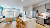 Located at 2125 Yale St in Houston's desirable 77008 zip code, this well-appointed 2-bedroom, 2-bathroom residence offers a thoughtfully designed single-floor layout. The open-concept living and kitchen area serves as the heart of the home, where light wood-tone flooring flows seamlessly throughout. The kitchen is equipped with stainless steel appliances, sleek gray flat-front cabinetry, a white quartz countertop island with built-in sink, and a dishwasher — all illuminated by track lighting. The living room features a bold teal accent wall, large French doors that invite abundant natural light and outdoor views, and a ceiling fan overhead. Both bedrooms are carpeted and generously sized, with large windows dressed in navy drapes. Each bedroom includes its own dedicated closet, with the primary suite offering a spacious walk-in closet and an en-suite bathroom featuring wood-toned cabinetry, white quartz countertops, and hardwood-style flooring. A second full bathroom serves the additional bedroom. A dedicated in-unit laundry room with full-size washer and dryer adds everyday convenience. Clean white walls and modern finishes throughout create a bright, contemporary ambiance.