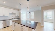 Located at 1020 Port Royal Trail in Myrtle Beach, SC, this single-story home offers a thoughtfully designed open-concept layout that seamlessly connects the kitchen, dining, and living areas. The kitchen is a standout feature, showcasing white shaker cabinetry, a subway tile backsplash, dark countertops, stainless steel appliances, and a central island with pendant lighting — ideal for both cooking and entertaining. Light hardwood flooring flows throughout the home, complementing the neutral color palette and creating a warm, cohesive atmosphere. The living area is bathed in natural light through multiple large windows dressed with white blinds, offering views of surrounding greenery. Both bedrooms are generously sized, each equipped with ceiling fans and large windows. The primary bedroom provides direct access to an en-suite area and benefits from exceptional natural light. Five closets, including a spacious walk-in with wire shelving, offer abundant storage. The bathrooms feature white cabinetry, dark countertops, and matte black fixtures. A dedicated laundry room adds everyday convenience. The overall design blends clean, modern aesthetics with functional living spaces throughout.
