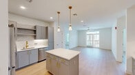 Located at 55 Summer St in South Walpole, MA, this well-appointed one-bedroom, one-bathroom residence offers a thoughtfully designed open-concept layout across a single floor. Light-toned hardwood-style flooring flows consistently throughout, lending a clean and cohesive aesthetic to every room.

The kitchen is a standout feature, showcasing gray cabinetry with gold hardware, a classic subway tile backsplash, white quartz countertops, stainless steel appliances, and a kitchen island with a light blue accent base topped with white quartz. Pendant lighting with gold fixtures adds a contemporary touch. The kitchen opens seamlessly into the living area, which is bathed in natural light from large windows and a glass balcony door. A ceiling fan and access to the private balcony with outdoor views complete the living space.

The bedroom is generously proportioned, featuring large windows overlooking the surrounding neighborhood, a ceiling fan with built-in lighting, and continued hardwood-style flooring. A dedicated closet offers wire shelving for organized storage.

The bathroom is elegantly finished with marble-style tile flooring, a double-sink vanity with gray cabinetry and gold fixtures, a large mirror with modern wall lighting, and a full soaking tub with gray subway tile surround.