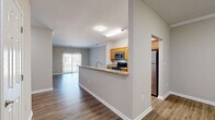 Located at 553 Settlers Landing Rd in Hampton, Virginia, this single-floor residence offers a thoughtfully designed layout that maximizes both functionality and comfort. The open-concept living and dining area is anchored by rich hardwood-style flooring and features elegant crown molding, with a full-length sliding glass door that floods the space with natural light and provides outdoor views. The kitchen is a standout feature, equipped with warm honey-toned cabinetry, granite countertops, a peninsula with a built-in sink, and a full suite of stainless steel appliances including a refrigerator, dishwasher, microwave, and range. This layout flows seamlessly into the dining and living areas, making it ideal for everyday living and entertaining. The spacious bedroom is finished with plush carpeting, neutral tones, and a large window that brings in natural light, complemented by generous closet space — including three closets total throughout the unit. The bathroom features a full tub-shower combination with white tile surround and hardwood-style flooring. A dedicated laundry area adds everyday convenience. The overall aesthetic is clean and modern, with a neutral color palette throughout.